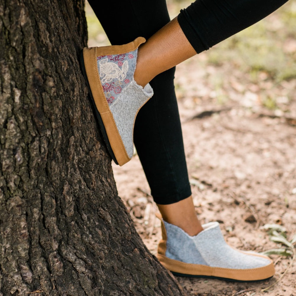 Women's Forest Bootie Slippers in Heather Grey Hare On Model Against A Tree#color_heather-grey-hare