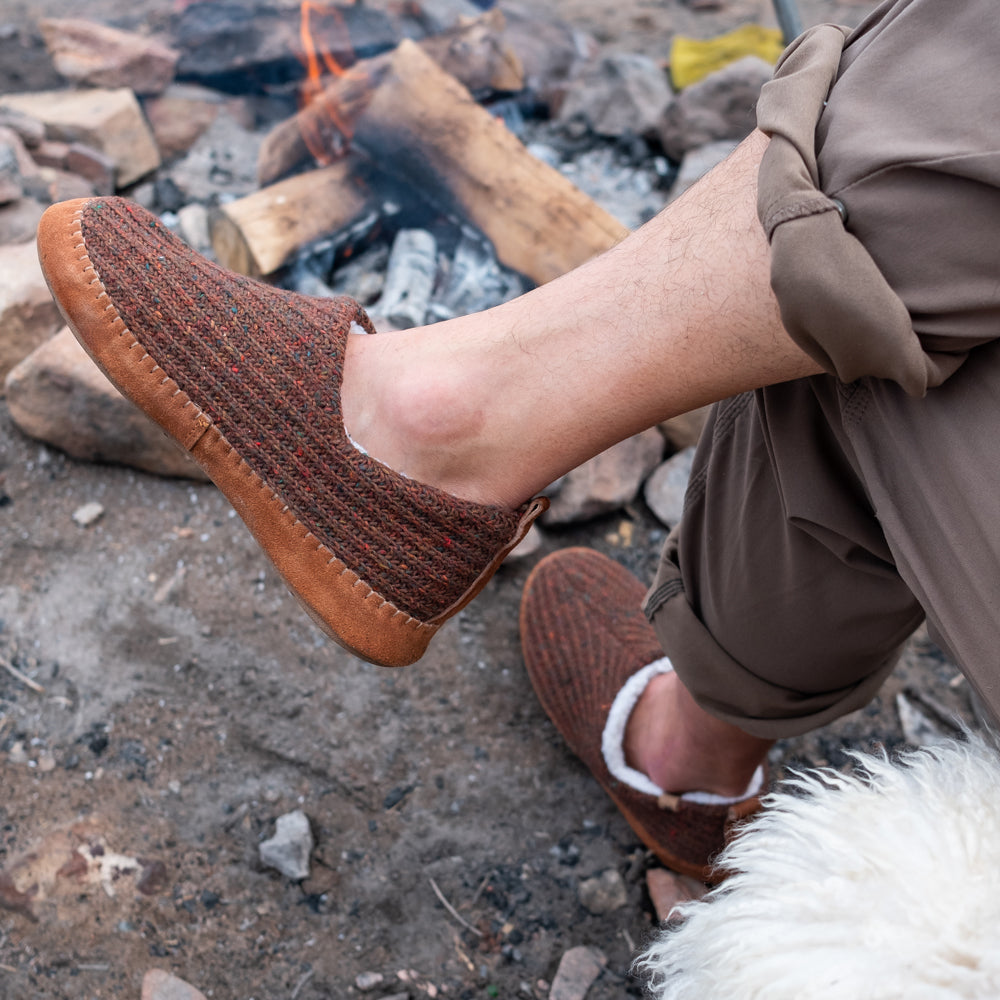 Men’s Sustainable Camden Moccasins on figure. Male model sitting with his legs crossed in front of a fire.#color_walnut